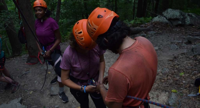 Two people wearing orange helmets work to tie knots